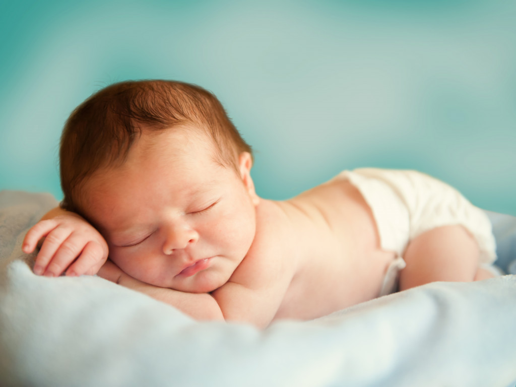 infant sleeping on top of a light blue green bedding