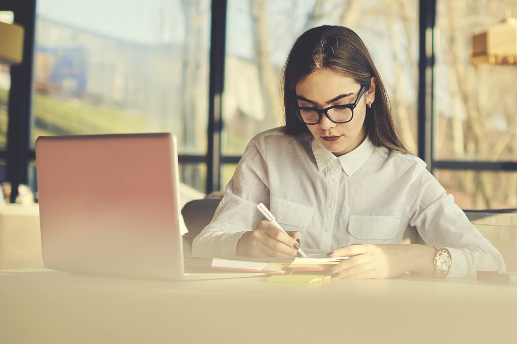 Woman entrepreneur writing while in front of laptop