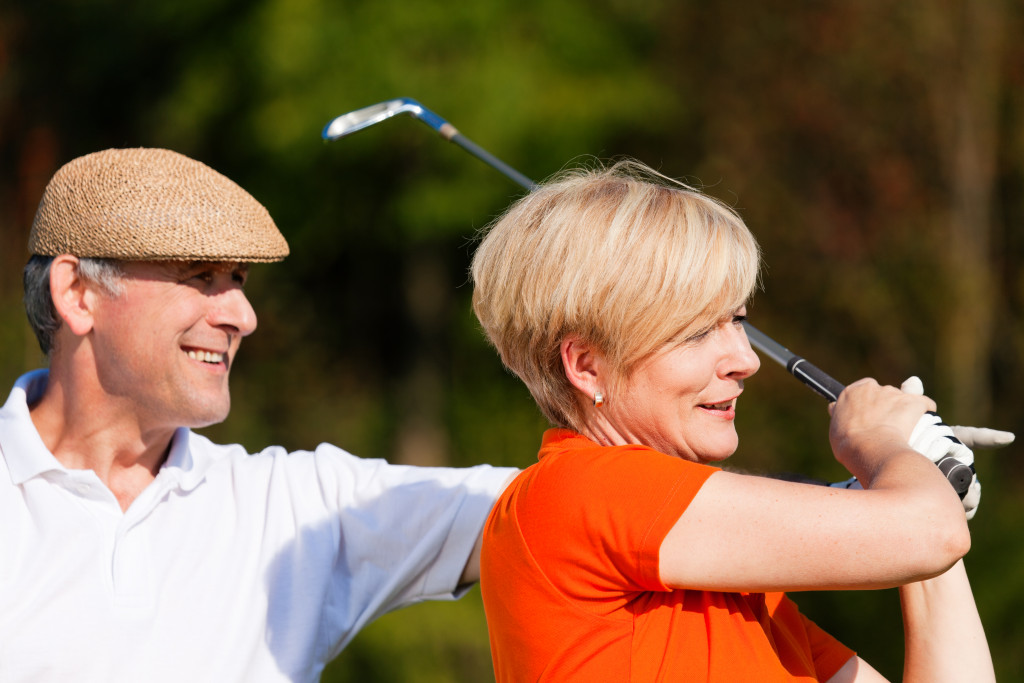 woman being assisted by a man in swinging a golf club