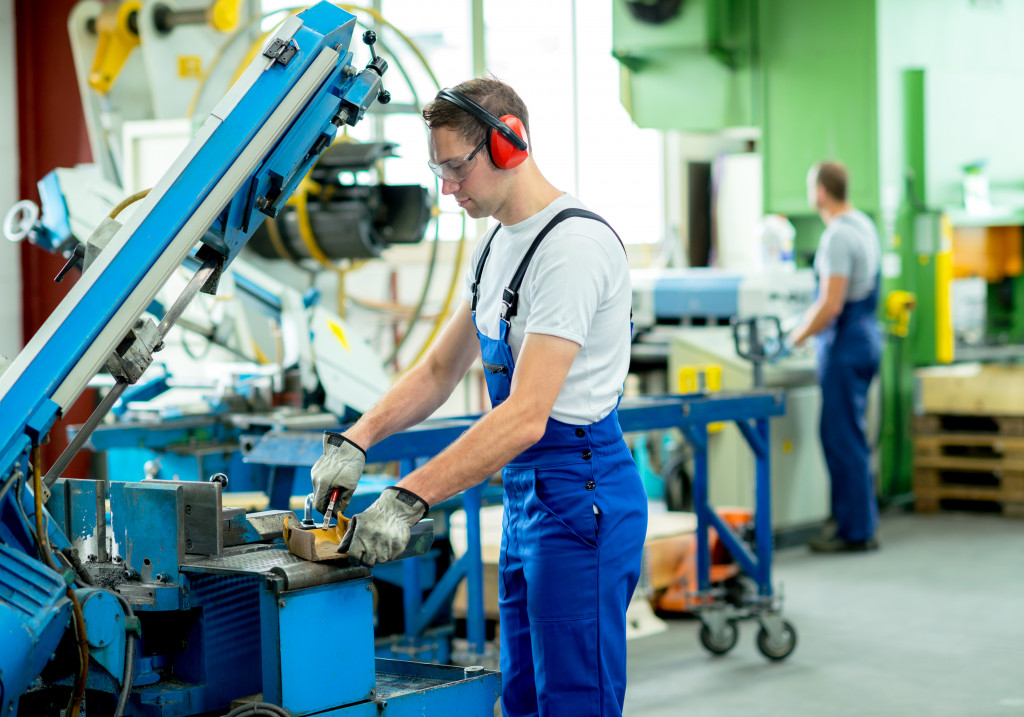 worker in protective clothing in factory using machine