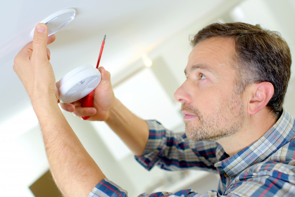 A man installing a smoke detector on the ceiling of a house
