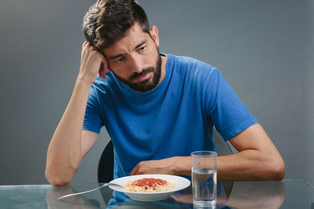 A sad man with no appetite sitting in front of a plate of spaghetti and a glass of water