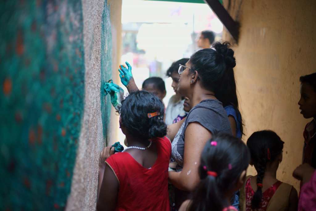 A woman painting on wall with small girls of ngo