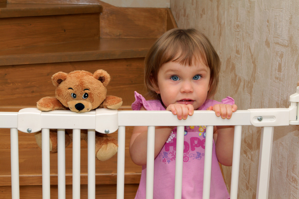little girl with her teddy in the stair gate