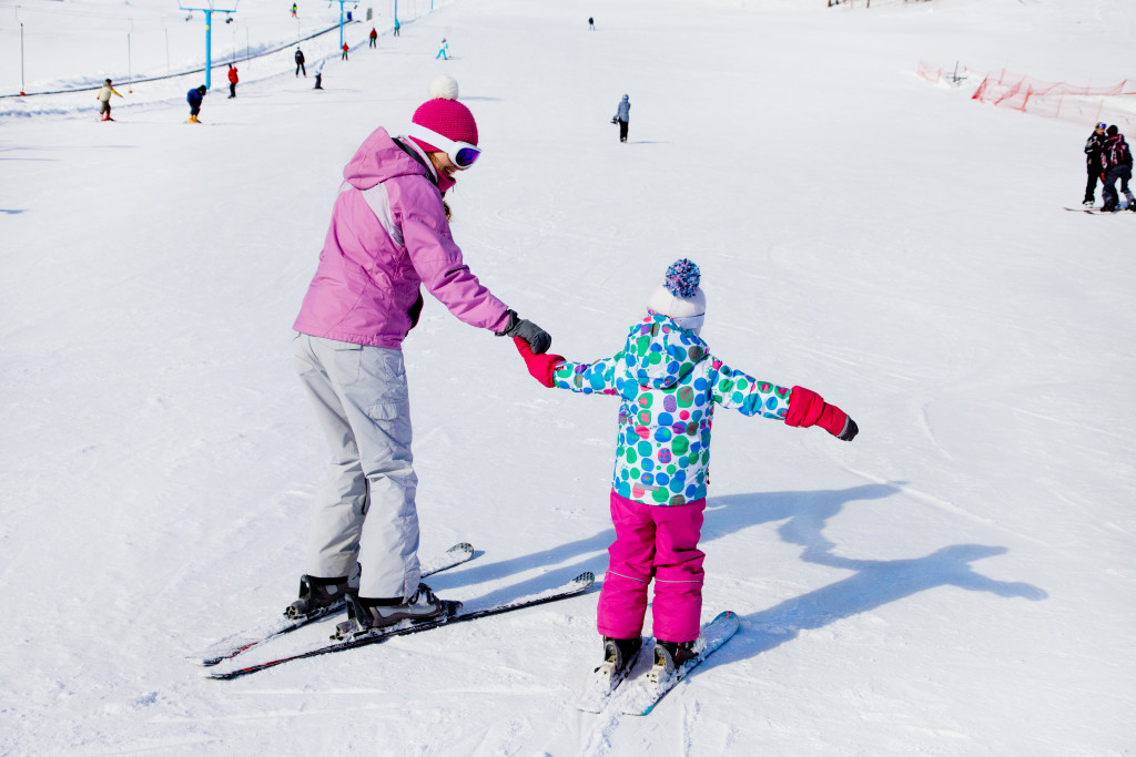 A mom holding her child's hand while they are skiing on a beginner slope wearing winterwear