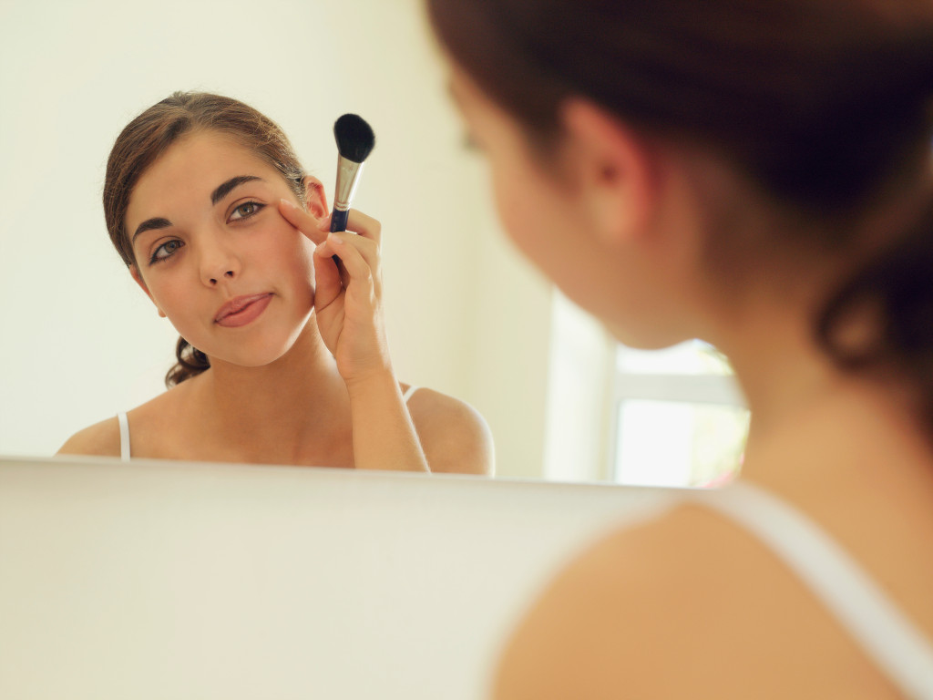 a young woman looking at the mirror applying a makeup using fingers and blush