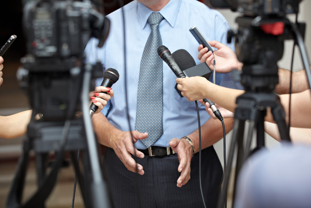 A company spokesperson is being interviewed by journalists with mics and cameras