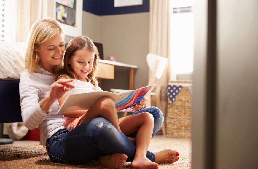 Mother reading a book with her daughter inside a room in the house.