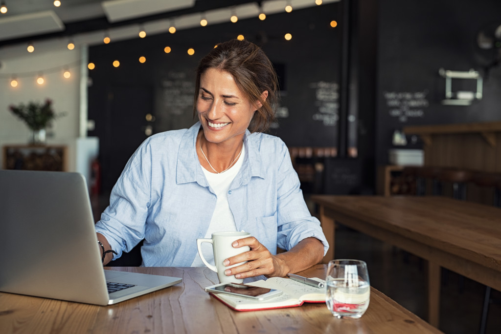 Young businesswoman smiling while holding coffee and checking her business using a laptop.