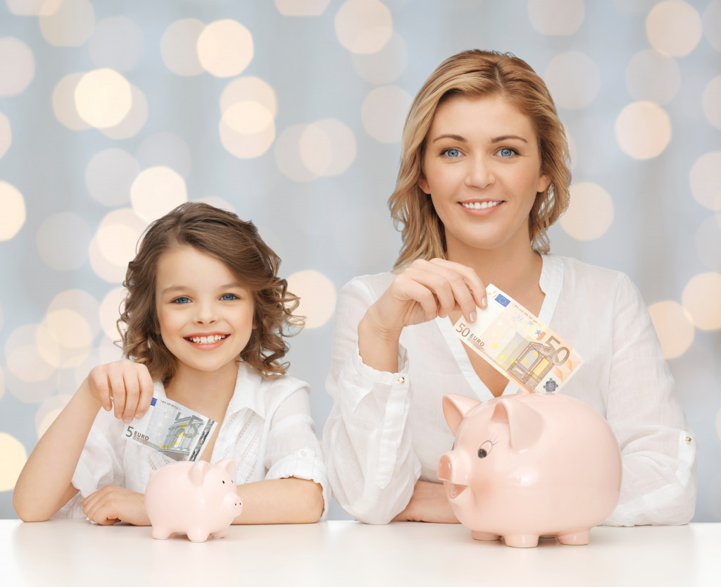 Mother and daughter placing bills on piggy bank