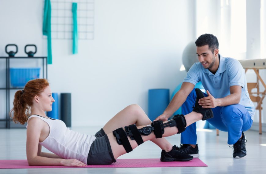 A woman lying on a mat with leg injury receiving treatment from a physical therapy