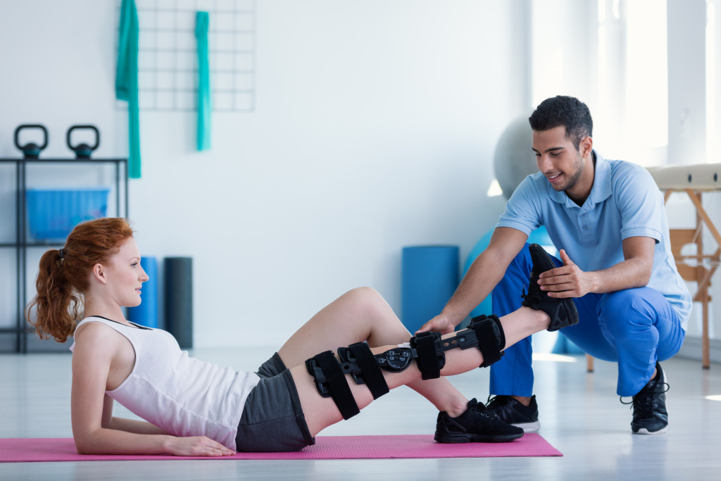 A woman lying on a mat with leg injury receiving treatment from a physical therapy